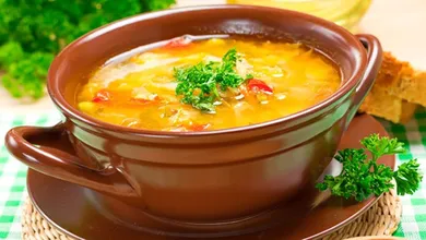 Receta tradicional de sopa de habas cocinándose en olla con cilantro y tomate.